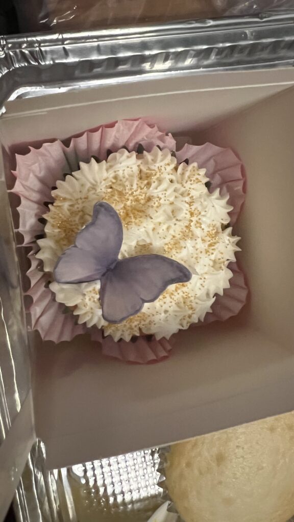 a buttercream frosted cupcake with gold dusting sugar and an edible rice paper butterfly on top