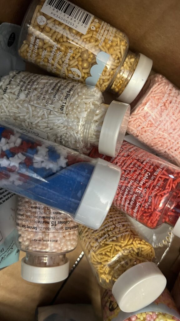 jars of assorted sprinkles and jimmies in different colors and flavors for toppings as well as dusting sugars